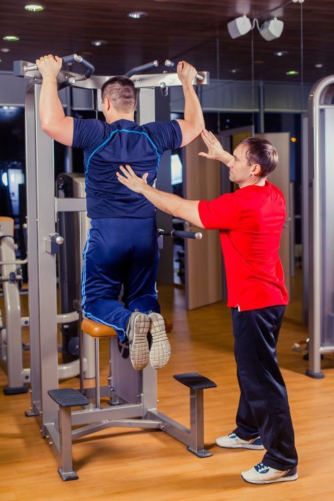 Man doing machine assisted pull ups with a trainer